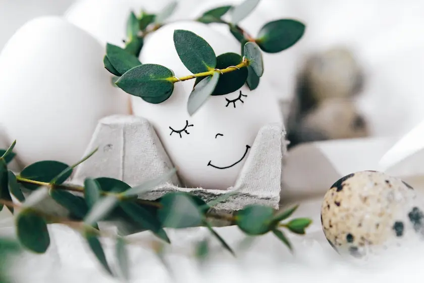 A white egg in an egg carton with a drawn face, crowned with a wreath 