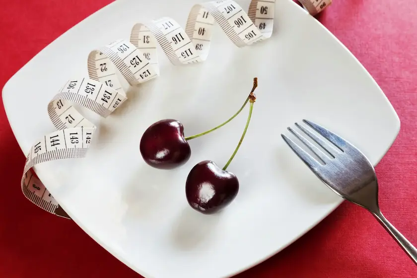 Two cherries and a measuring tape in a white plate.