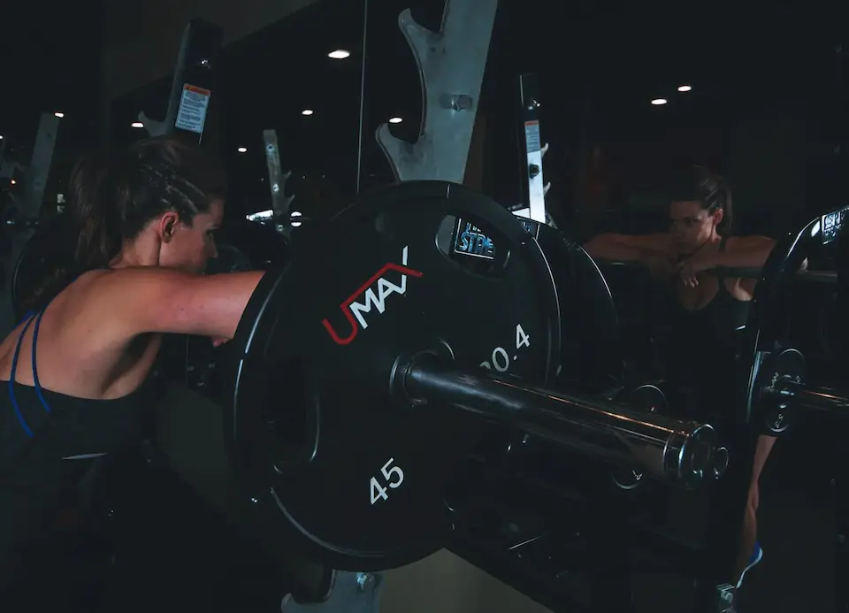 A fit woman standing at the squat rack, staring with focus at her reflection in the mirror.