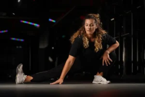 A fit, attractive woman in her 40s, stretching her right leg on the floor.